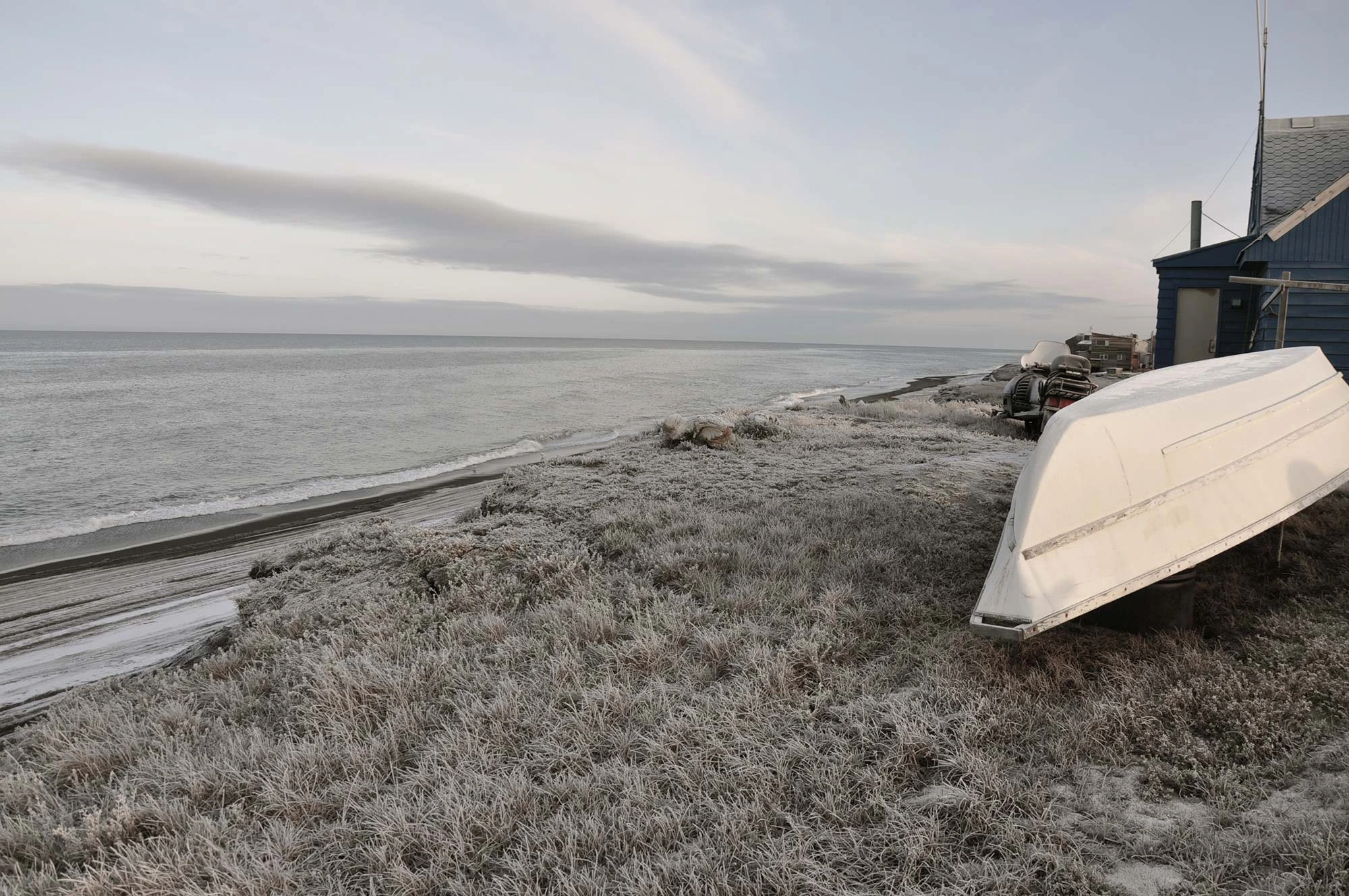 A white boat and a blue shack, sitting on a grassy cliff overlooking the ocean